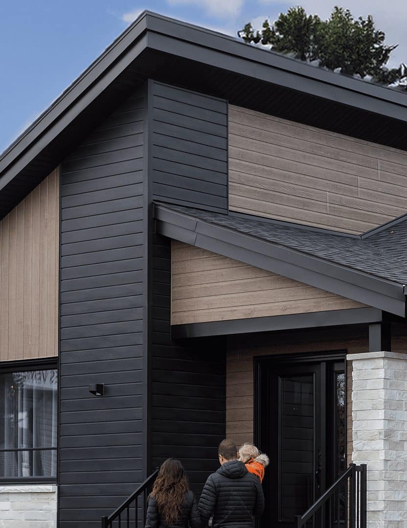 Maison préfabriquée plain-pied du modèle Tryka de style contemporain. Vue de l'extérieur avant. Un couple se dirige vers l'entrée.