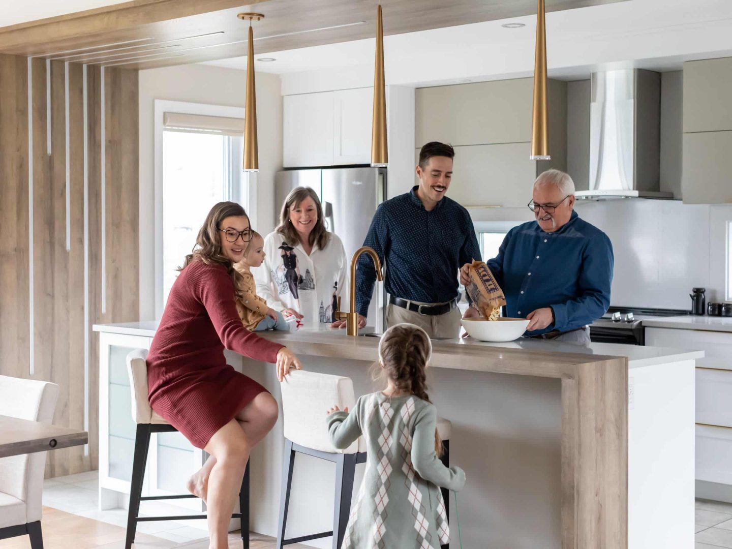 Family with one child and two grandparents around a kitchen's table. Grandfather pours popcorn into a bowl.