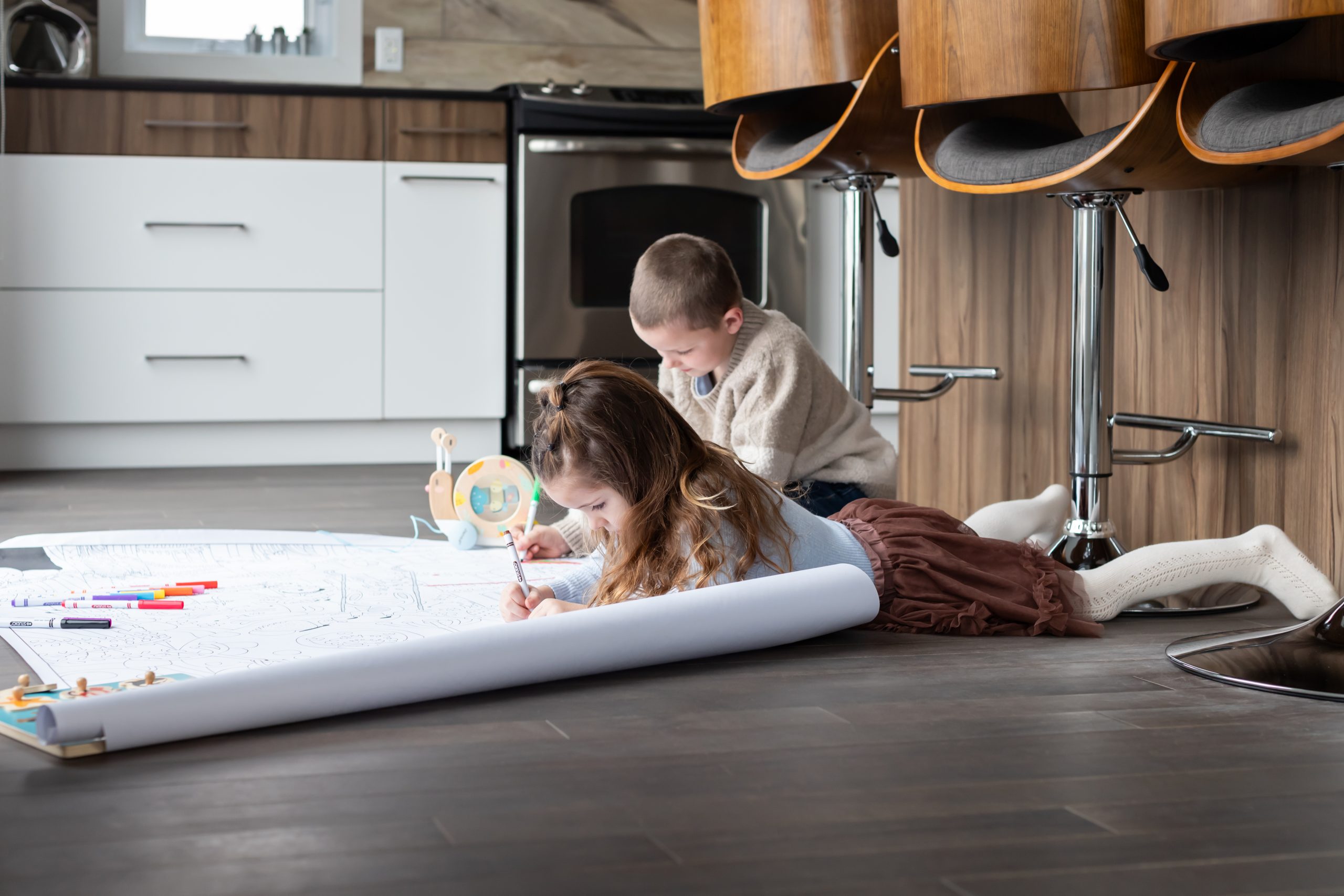 deux enfants qui dessinent au sol sur une grande feuille.
